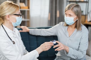 여성 의료 종사자, 의사 또는 간호사, 손가락 맥박 산소 측정기를 사용하여 집에서 아픈 환자 노인 여성을 방문하여 산소 수준을 확인합니다.