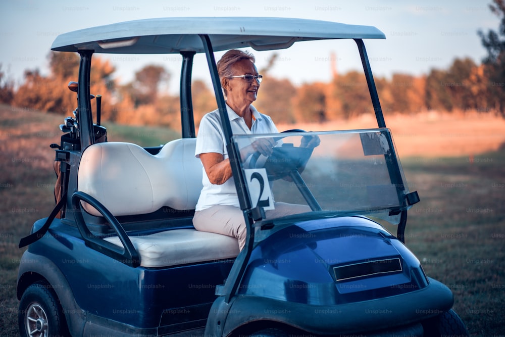 Donna anziana in sella a un'auto da golf.