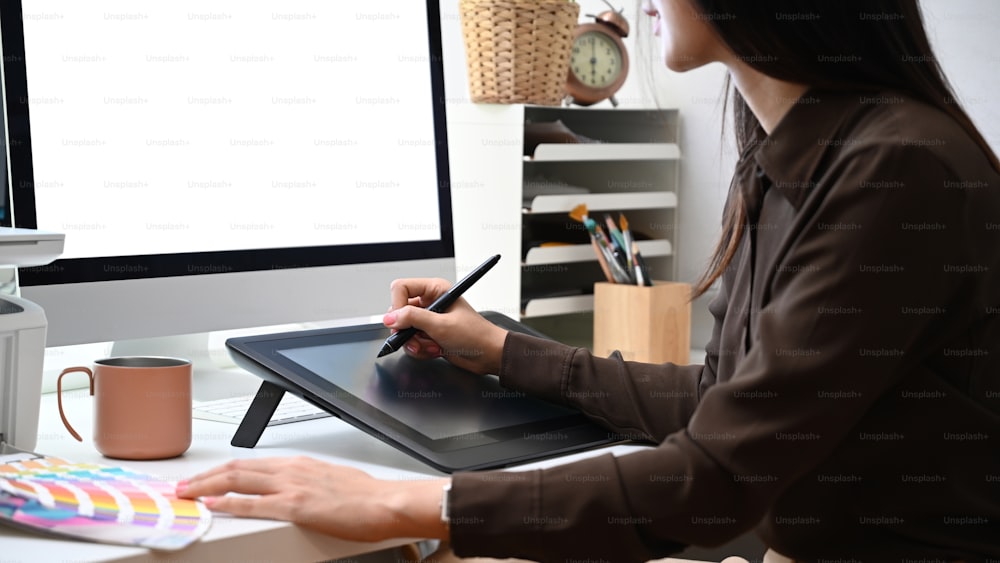 Vue latérale d’une graphiste femme créative travaillant avec une tablette graphique et un ordinateur au bureau.