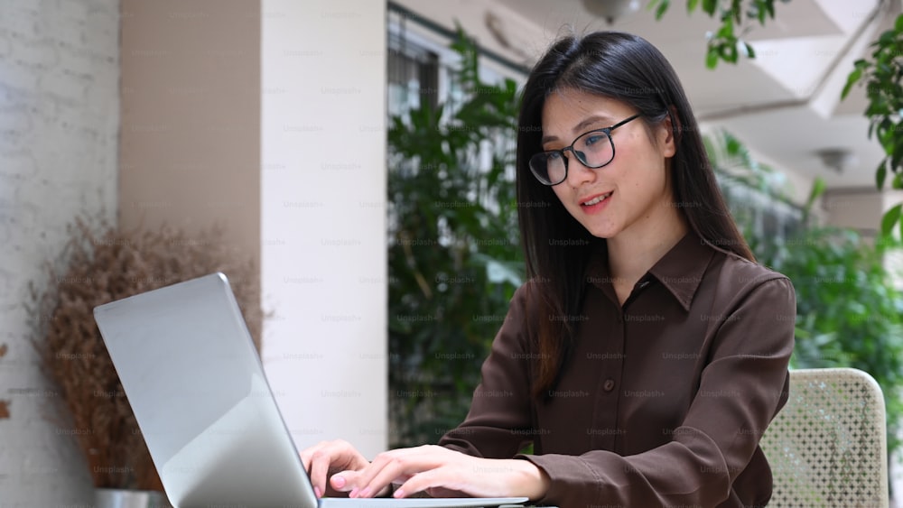 웃고 있는 젊은 여성이 컴퓨터 노트북으로 일하거나 인터넷을 서핑하고 있다.