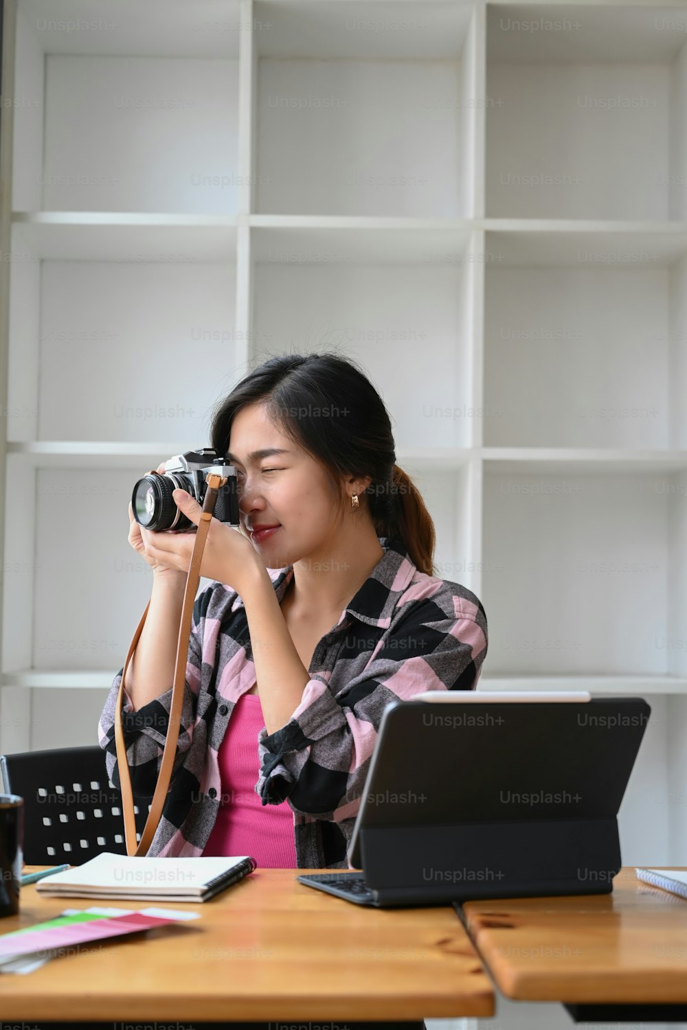 Portrait of young female photographer sitting in front of computer tablet and setting up her camera in modern office.