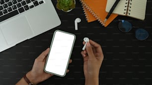 Above view of woman hand holding smart phone and wireless earphone on black leather.