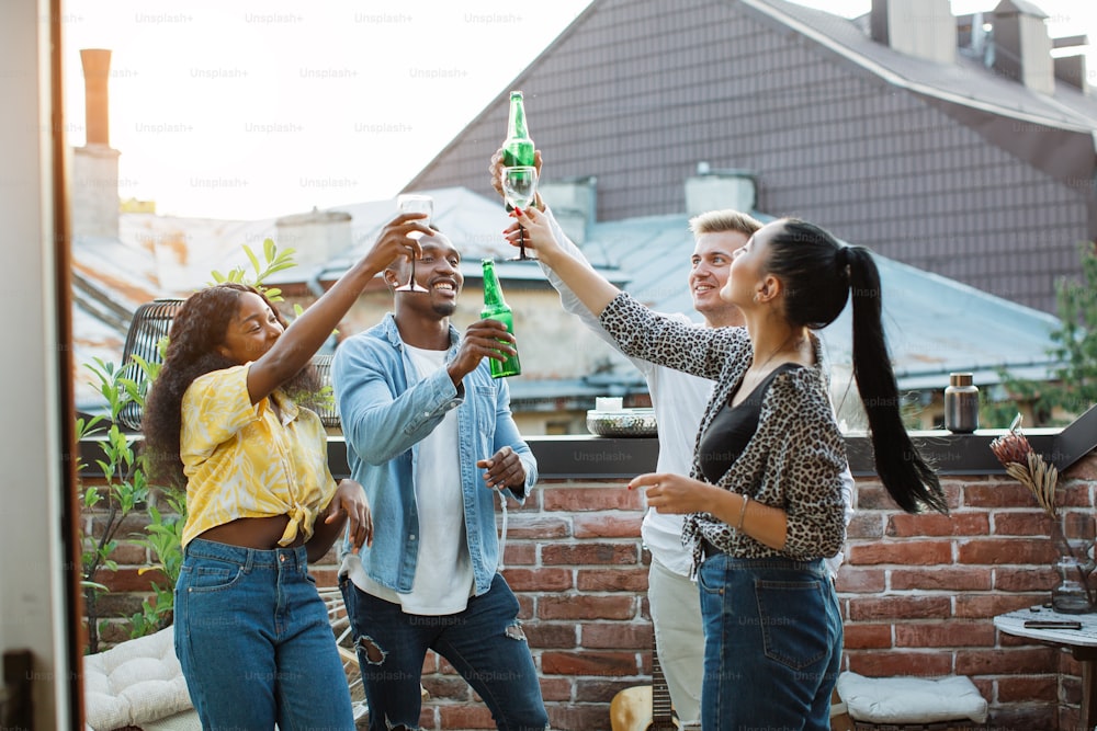 다민족 친구들이 옥상에서 춤을 추고 휴식을 취하고 있습니다. 술을 마시고 채팅하는 젊은 힙 스터를 그룹화합니다. 평온한 주말.