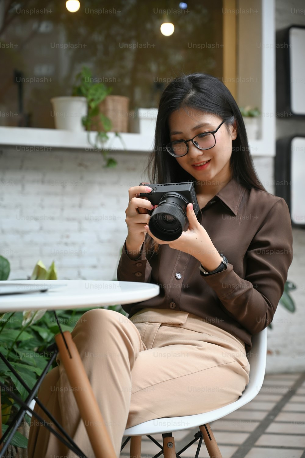 Porträt einer lächelnden jungen Frau, die im Café im Freien sitzt und das Bild ihrer Dirialkamera überprüft.