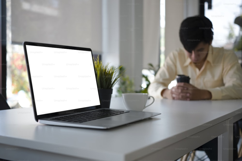 白いオフィスの机に空の画面と背景に座っているビジネスマンとコンピューターのラップトップの接写。