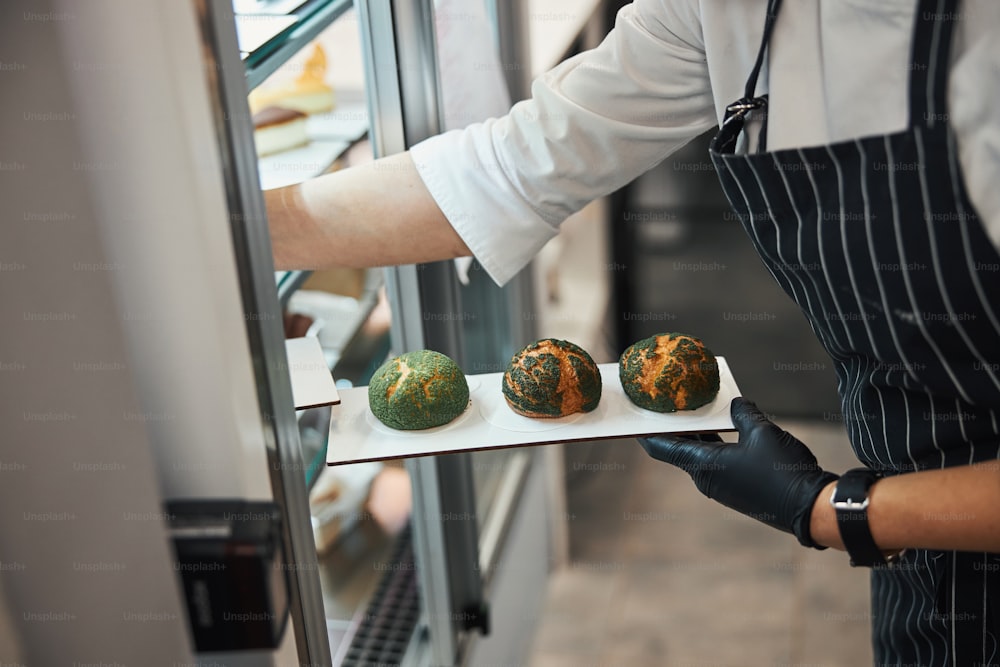 Foto ritagliata di chef indaffarato che mette un piatto con focaccine fresche sul display del caffè