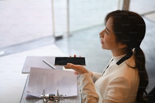 Mujer de negocios exitosa sentada en un lugar de trabajo moderno y hablando por altavoz.