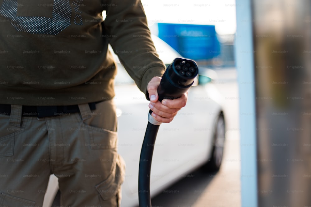 Man pours fuel into his car. Focus is on hand.  Electric pump for car.