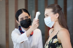Les clients heureux vérifient la fièvre à l’aide d’un thermomètre numérique pour scanner et protéger contre le coronavirus COVID-19 à la réception de l’hôtel
