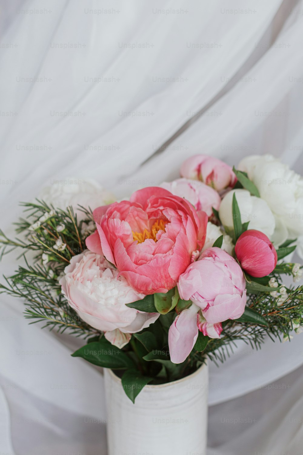 Beautiful stylish peonies bouquet on background of soft white fabric. Pink and white peony flowers in ceramic vase on pastel rustic background. Happy Mothers day. Modern bridal bouquet