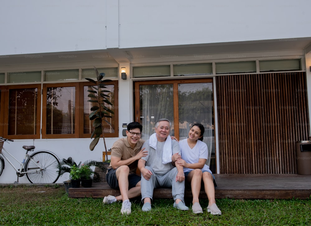 Portrait of Happy Asian family enjoy exercising together at home. Senior father with adult daughter and son enjoy workout together in the garden. Retirement elderly male with son spending time together with weekend activity.