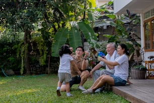 집에서 함께 운동하는 행복한 아시아 다세대 가족. 아버지, 어머니, 할아버지는 귀여운 딸과 함께 휴식을 취하고 아침에 집 앞마당에서 놀고 운동하며 즐거운 시간을 보냅니다.