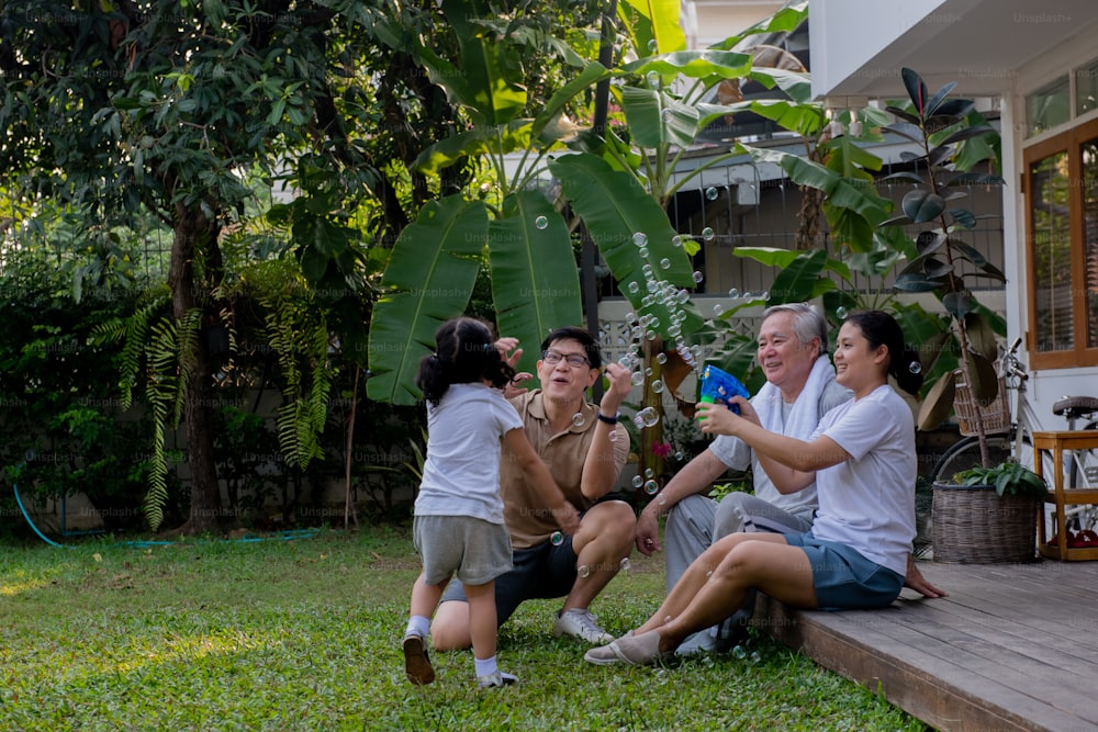 Happy Asian multi-generation family exercising together at home. Father, mother and grandfather with cute baby girl relax and having fun playing and exercising at home front yard in the morning.