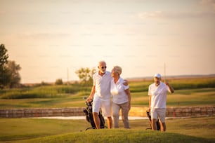 Três golfistas seniores. O foco está no homem e na mulher.