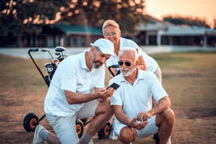 Golfistas seniores em quadra. Dois homens usando o telefone inteligente.
