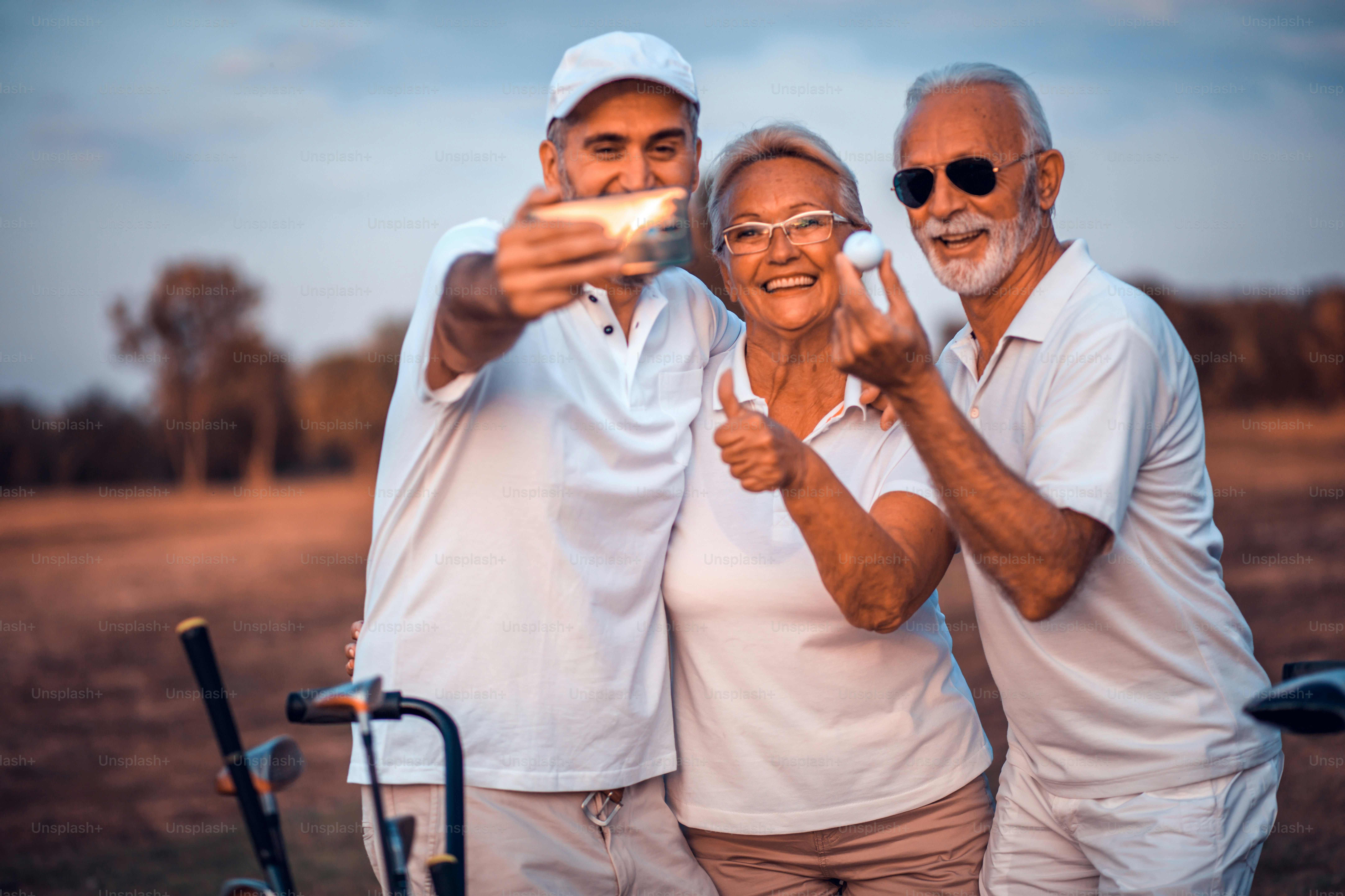 Senior golfers using phone and taking self portrait. Focus is on background