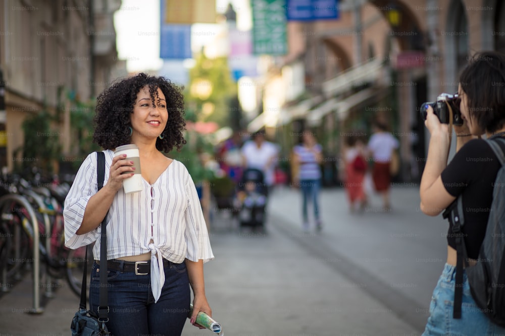 Ótima foto.  Mulher sorridente em pé na rua com xícara de café. Mulher tirando foto dela.