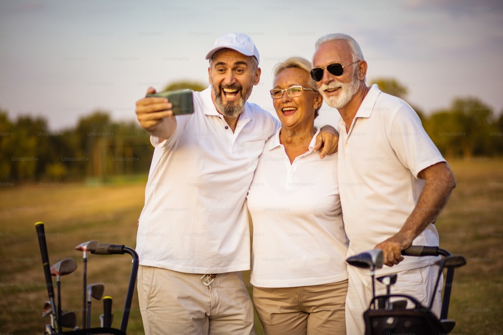 Golfeurs seniors utilisant leur téléphone et prenant un autoportrait. L’accent est mis sur l’arrière-plan.
