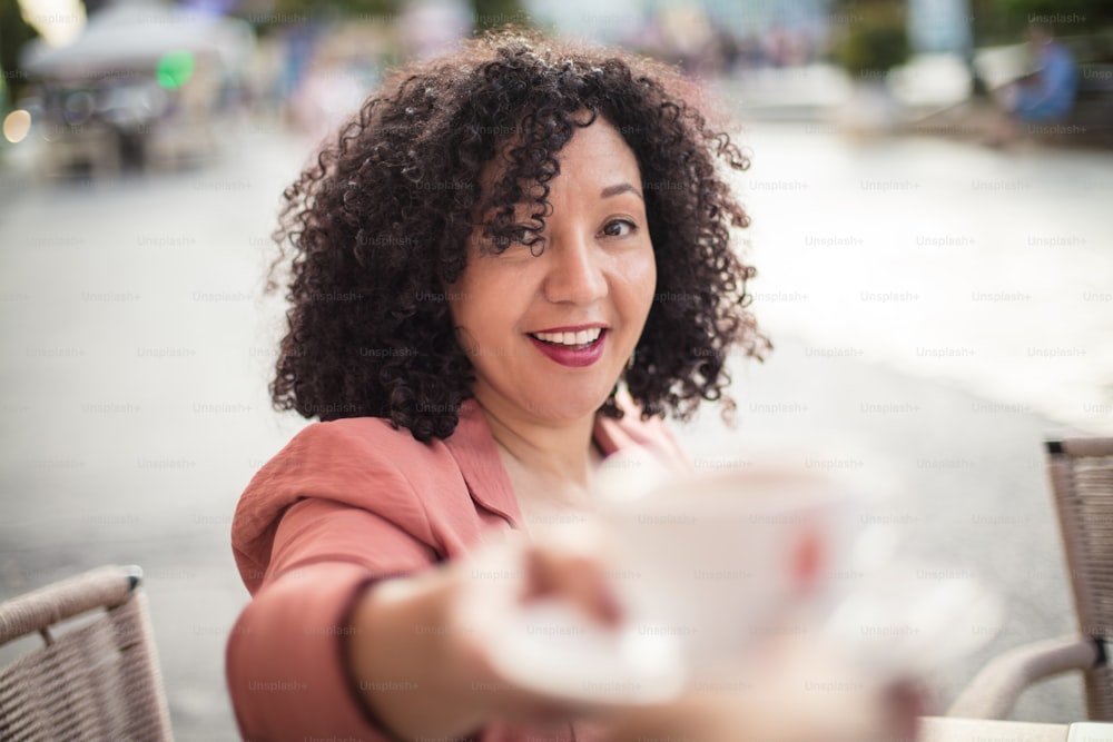 Smiling woman at café taking mug of coffee. Focus is on background.