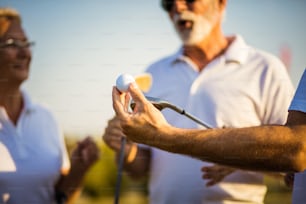 Senior friends on golf court talking. Focus is on hand.