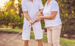 Seniorenpaar beim gemeinsamen Golfspielen. Mann hilft Frau im Spiel.