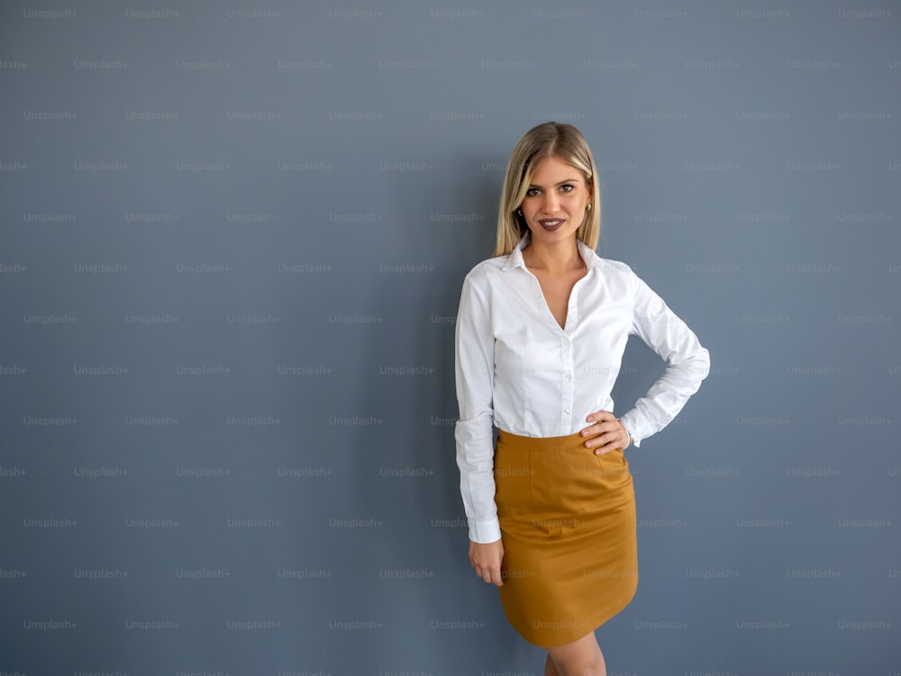 Retrato de uma mulher de negócios jovem bonita em pé contra o fundo cinzento no escritório