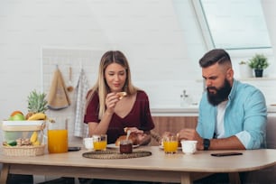 Jeune couple attrayant prenant un petit-déjeuner dans la cuisine à la maison