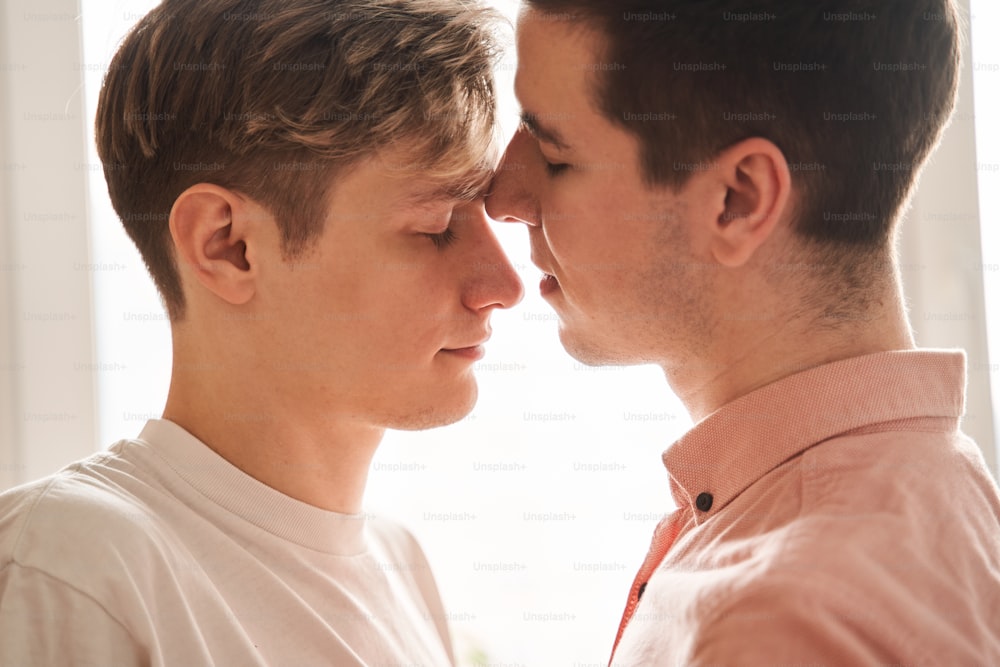 本当の愛。彼氏と一緒に台所に立っている間、目を閉じたままの親切な男の子の肖像画。LGBTのゲイカップルは瞬間と幸福のコンセプトを愛しています