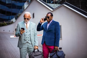 Two business men outdoors using smart phone.