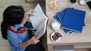 Above view of young asian girl reading book while sitting on floor in living room.