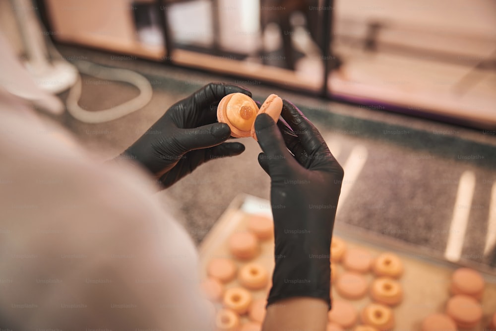 Cropped photo of chef in gloves connecting two parts of a macaron together