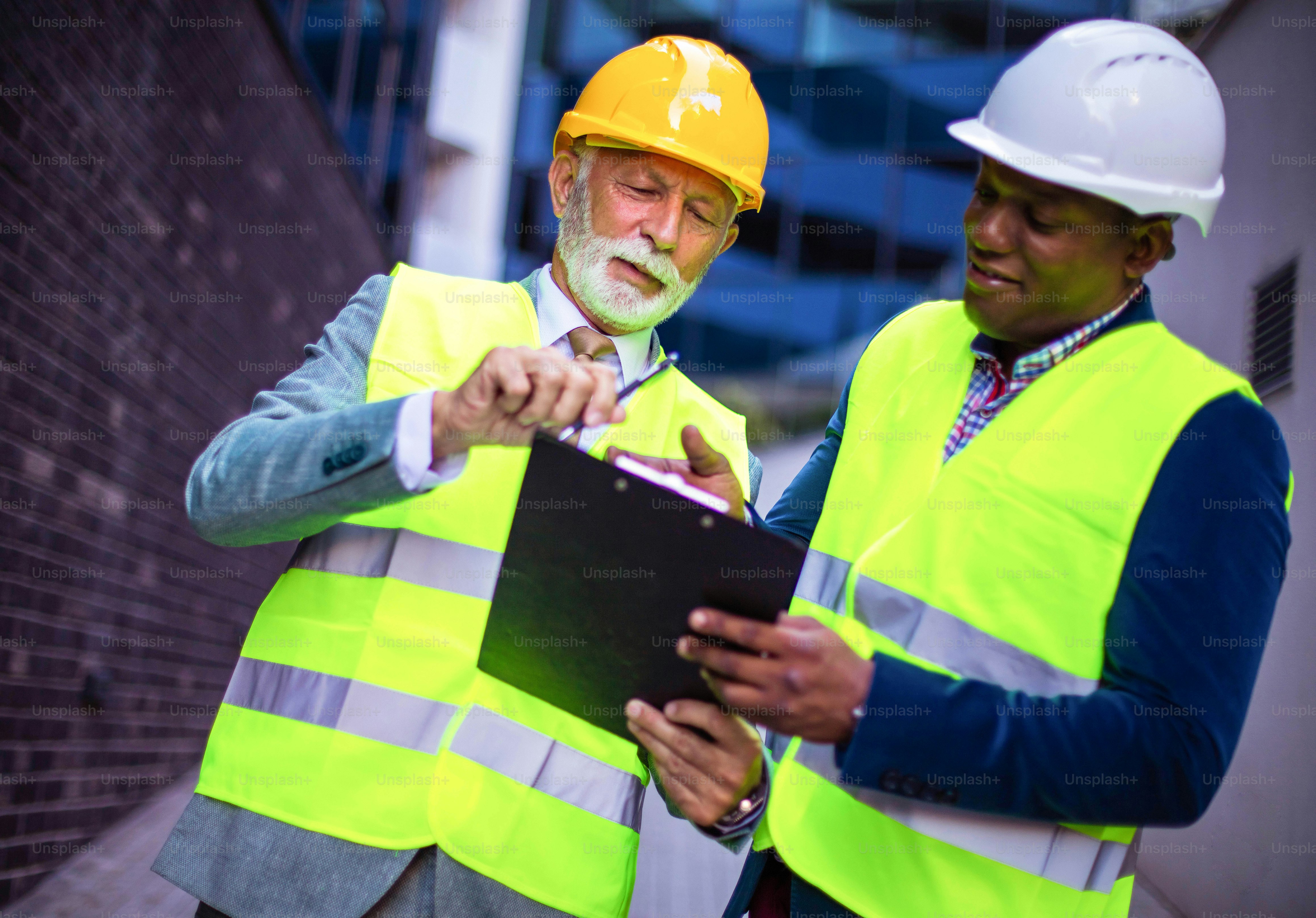 Mature engineer discussing the structure of the building with architects colleague at construction site. Reading document.