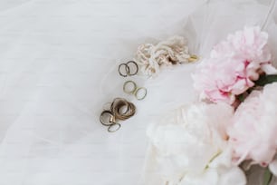 Stylish vintage accessories on soft tulle fabric with peony bouquet. Beautiful modern jewelry and pink and white peony flowers. Bridal morning. Feminine essentials
