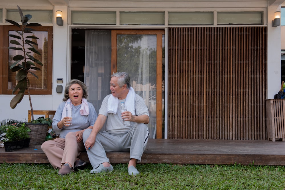 Happy Asian family exercising together at home. Senior couple drink water after do workout exercise together at home front yard in the morning. Retirement old age man and woman enjoy leisure activity at home