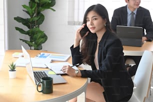 attractive businesswoman sitting with her colleague in office and making business call.