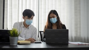 Young asian business people in protective mask discussing business idea and working together in office.