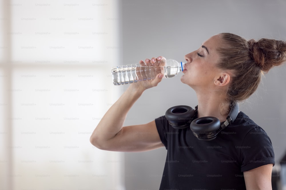 Portrait of beautiful young fit woman drinking water during traning in the gym.