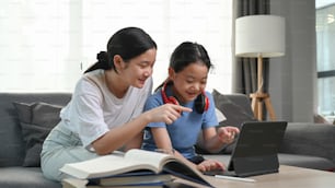 Two young girls sitting on sofa and watching something funny on digital tablet together.