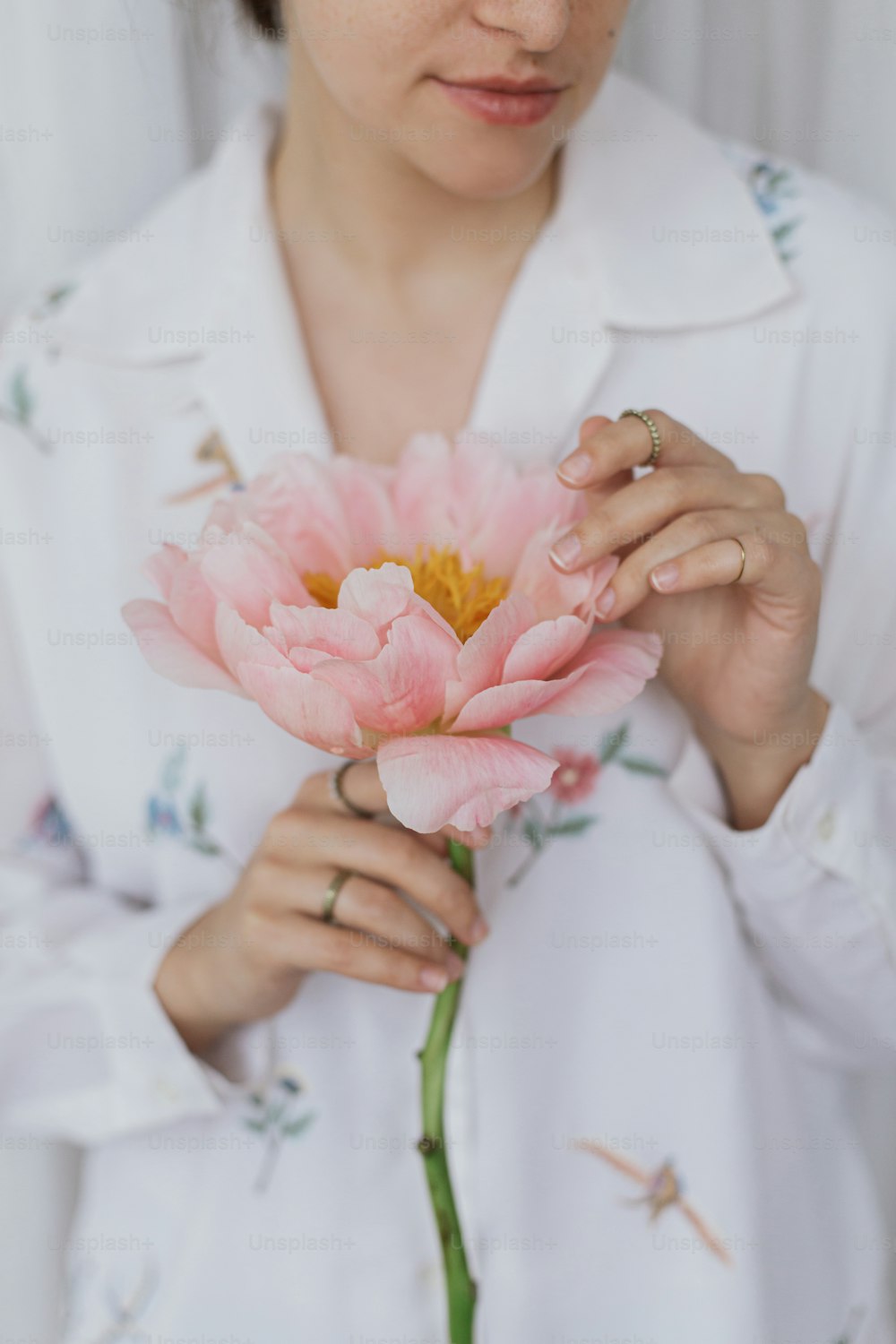 Beautiful stylish woman holding pink peony. Young female in boho floral shirt gently holding big peony flower in hands. Sensual soft image. Spring aesthetics