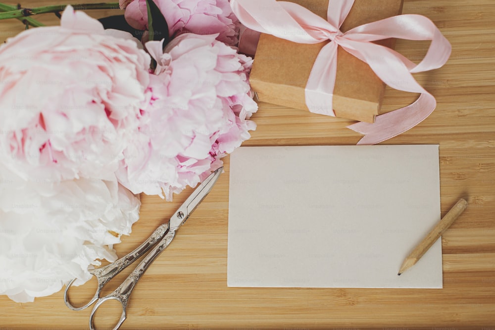 美しい牡丹の花束、スタイリッシュなギフトボックス、グリーティングカード、木製の背景にはさみ、コピースペース付きの上面図。幸せな母の日。ピンクと白の牡丹とプレゼント
