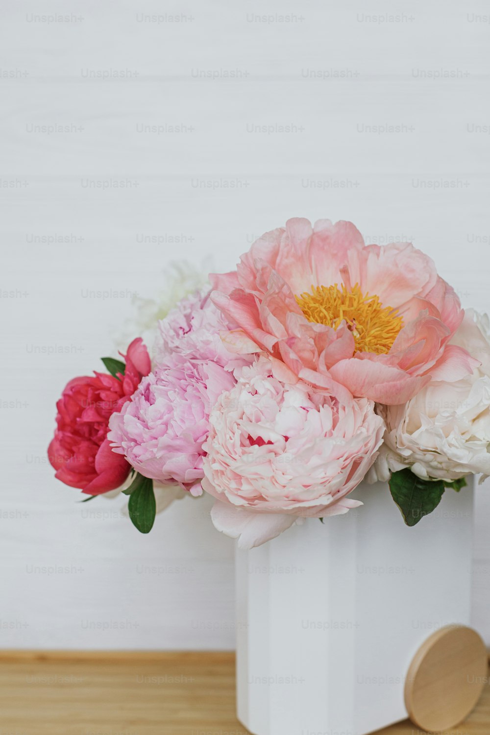 Beautiful peonies bouquet in modern stylish vase on white wooden background, copy space. Happy Mothers day. Womens day. Big pink and white peony flowers in room