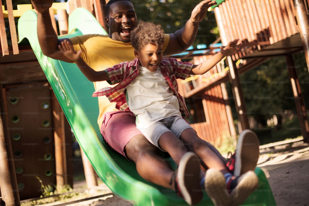 Toboggan time.  African American dad playing with son on playground.