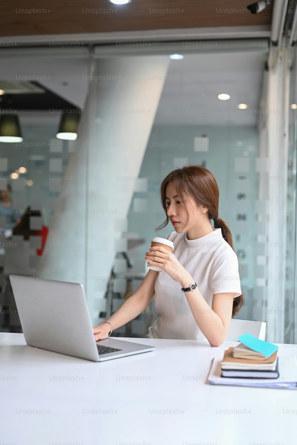 Portrait of pleasant businesswoman holding coffee cup and working on laptop computer.