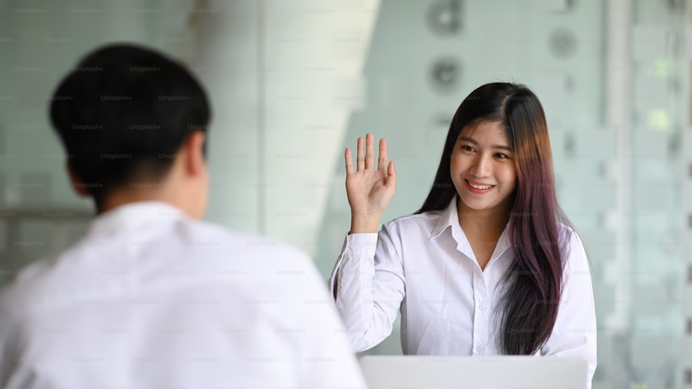 Cheerful young woman office worker greeting her colleague in modern office.