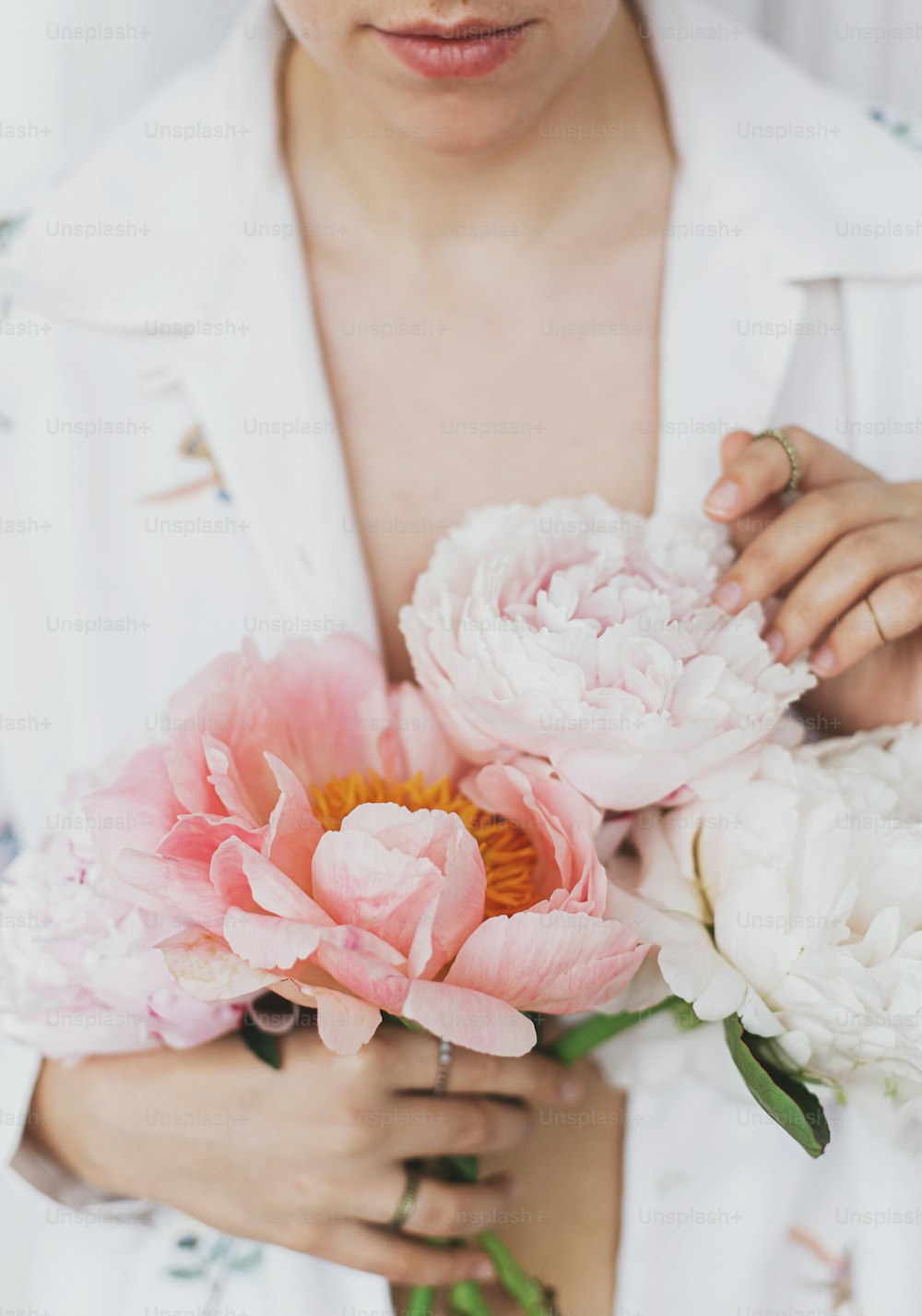 Schöne stilvolle Frau mit Pfingstrosenstrauß. Junge Frau im Boho-Blumenhemd, die sanft rosa und weiße Pfingstrosenblüten in den Händen hält. Sinnlich weiches Bild. Frühlingsästhetik