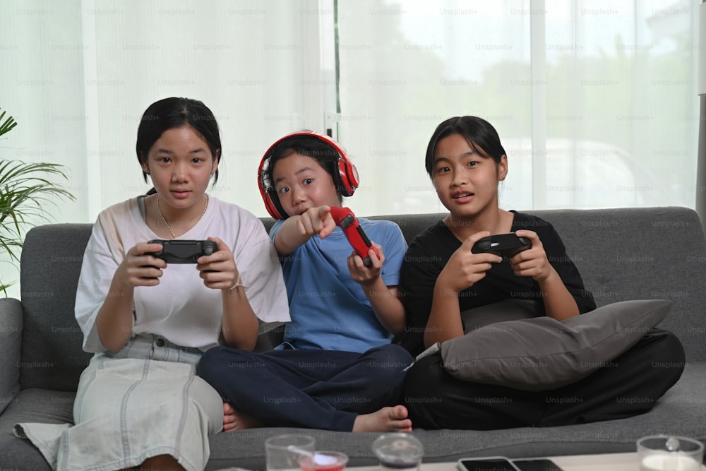 Young Asian girls playing video games and sitting together on cozy sofa in living room.