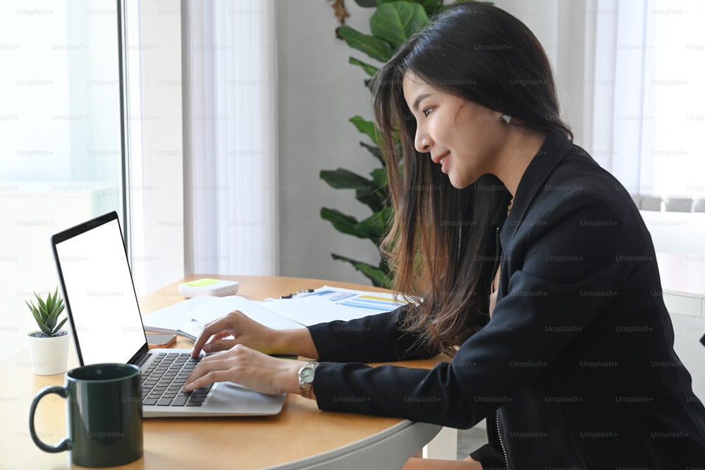 Side view of confident businesswoman working with laptop computer in modern office room.