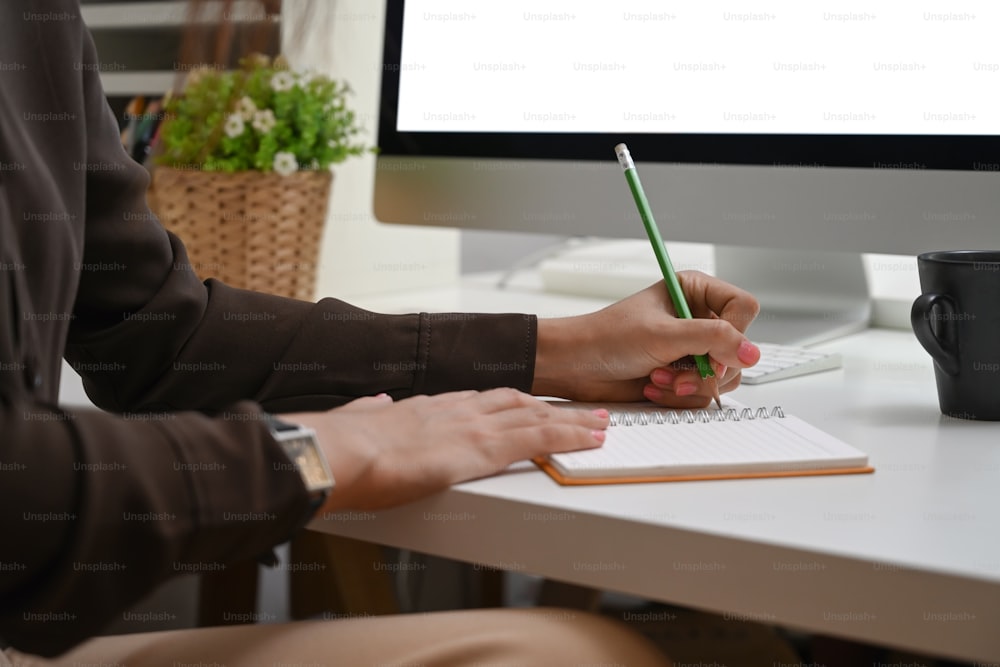 Ausschnittaufnahme einer jungen Frau, die am Schreibtisch des Heimbüros sitzt und den Arbeitstag auf ihrem Notebook plant.