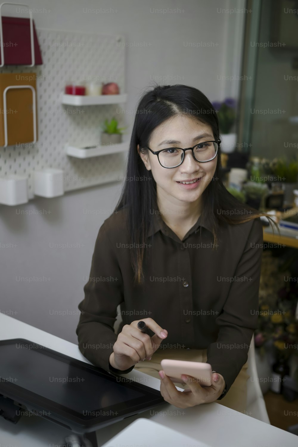 Ritratto di graphic designer donna felice che si siede al suo lavoro e tiene il telefono cellulare.
