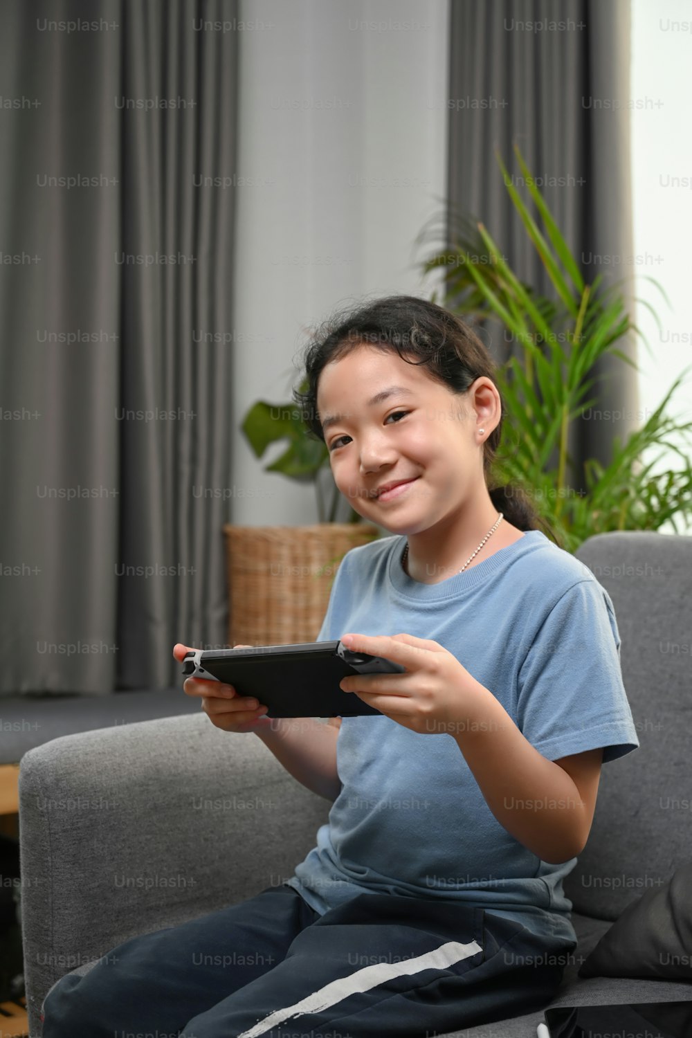 Retrato de una niña feliz jugando a un videojuego mientras está sentada en el sofá de su casa.